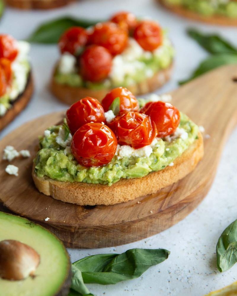 Avocado Toast with Sliced Tomatoes and Crumbled Feta Cheese on a Wooden Board