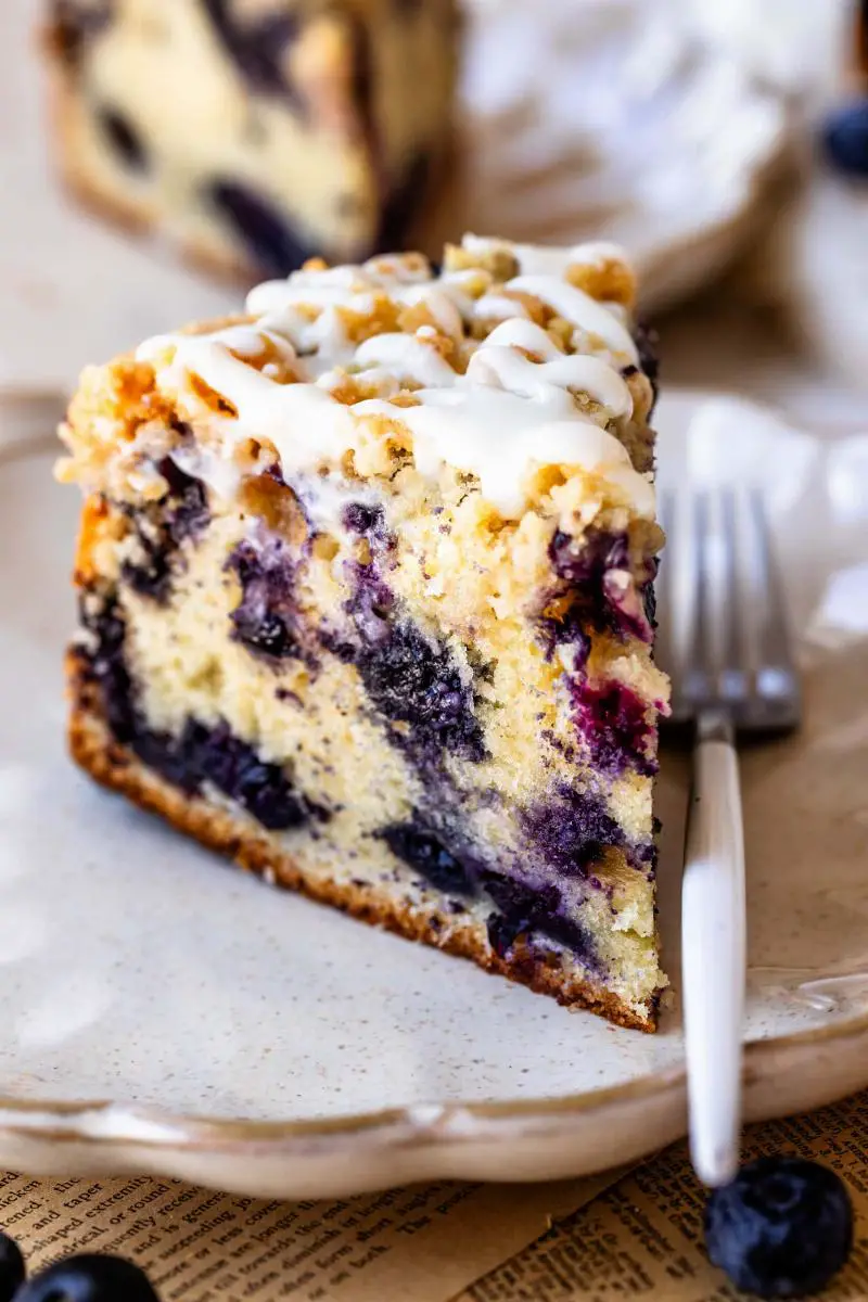 A slice of keto mixed berry cake with a light lemon-lime glaze, showing berries embedded in the crumb and the glaze drizzled on top.