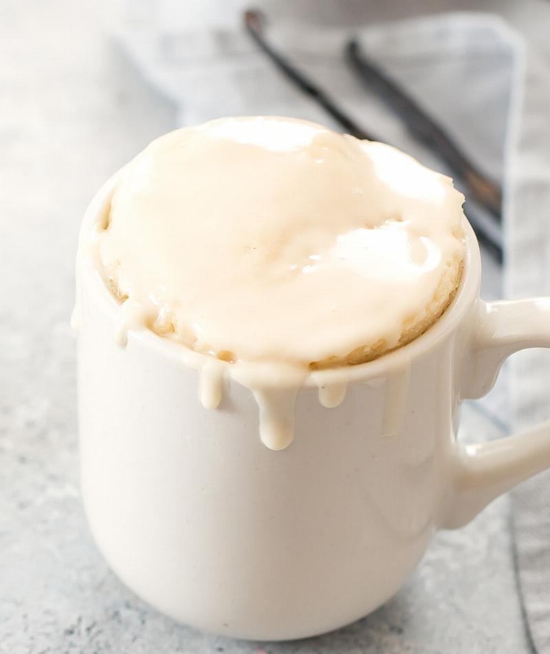 A light and fluffy keto vanilla bean mug cake baked in a mug, topped with whipped cream